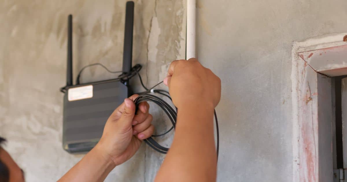 Person installing or adjusting a black Wi-Fi router on a wall, handling a cable.