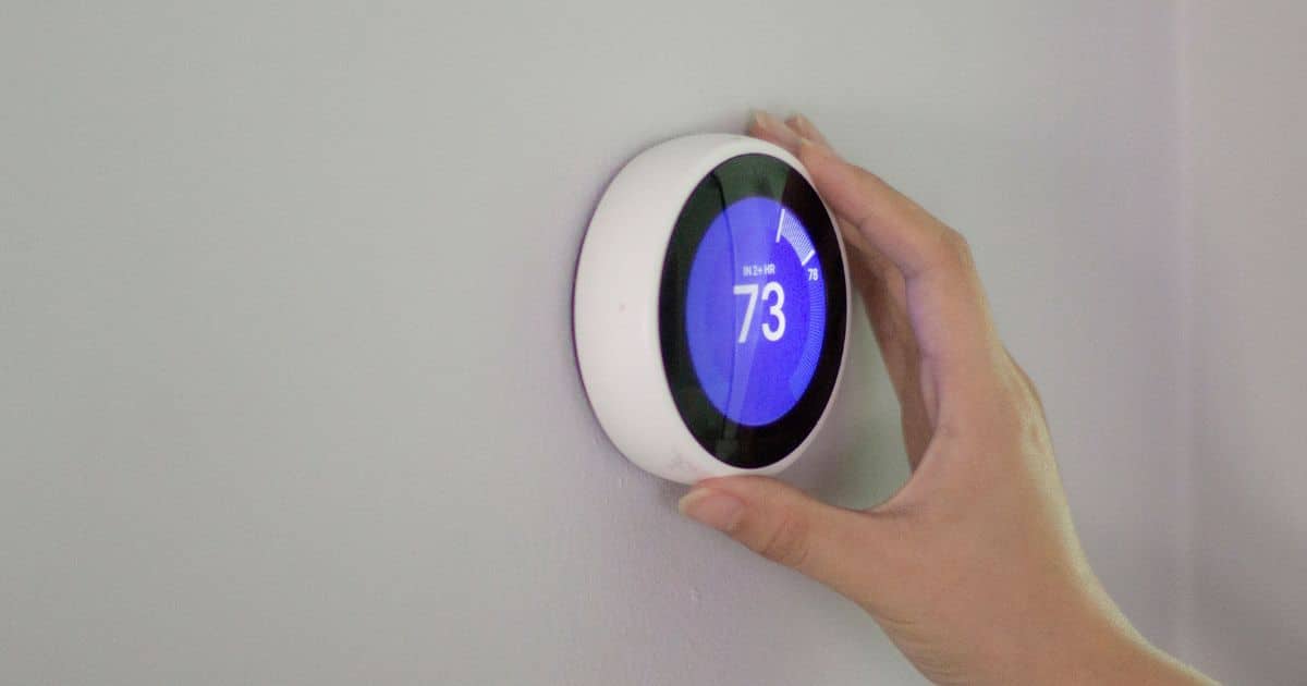 A person's hand adjusting a modern smart thermostat, designed with mechanical engineering principles, set to 73 degrees on a wall.