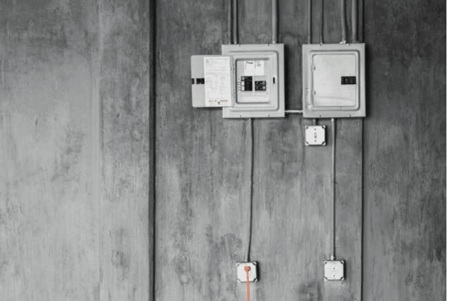 Two electrical panels and several wall outlets mounted on a grey concrete wall with visible wiring.