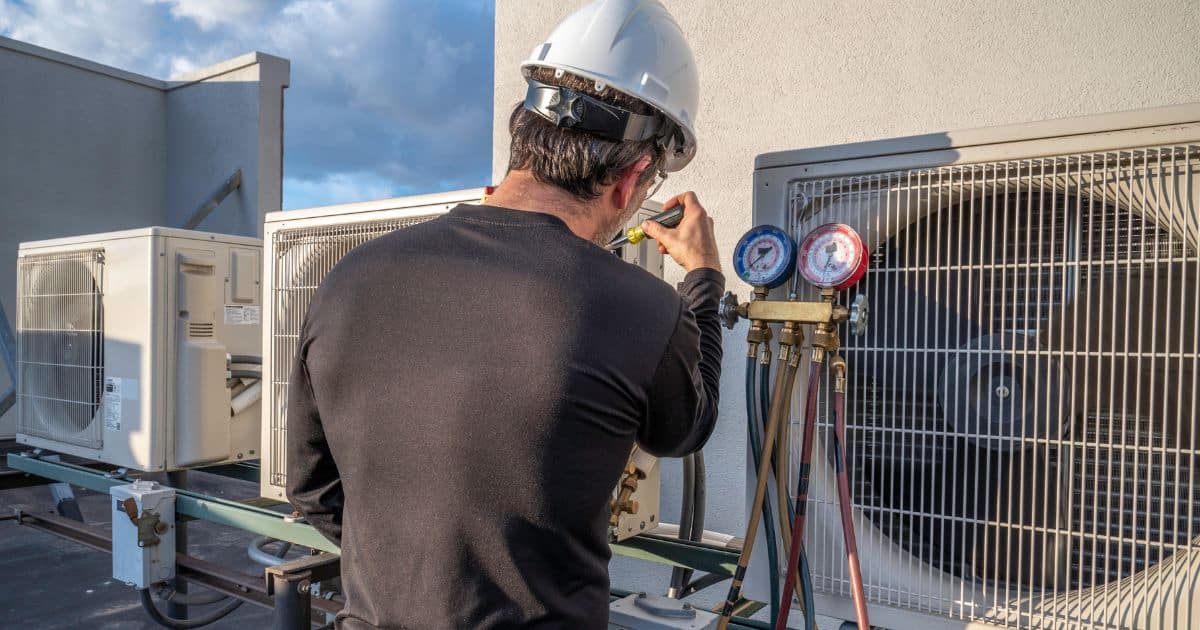 An hvac technician checks the pressure gauges on an outdoor air conditioning unit.