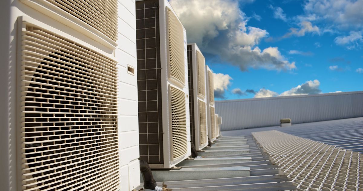 Row of air conditioning units on a building rooftop under a blue sky with clouds.