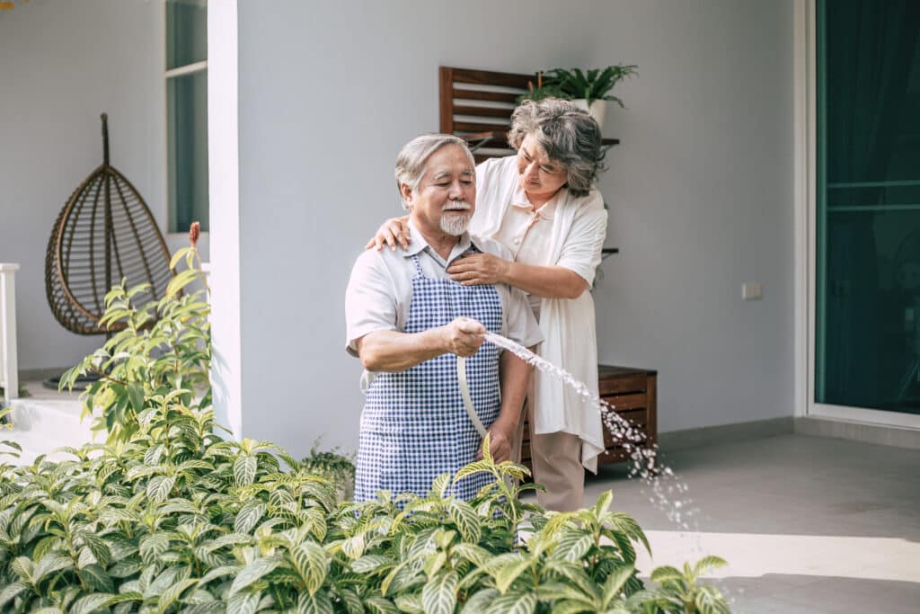 An elderly couple is watering plants in their home.