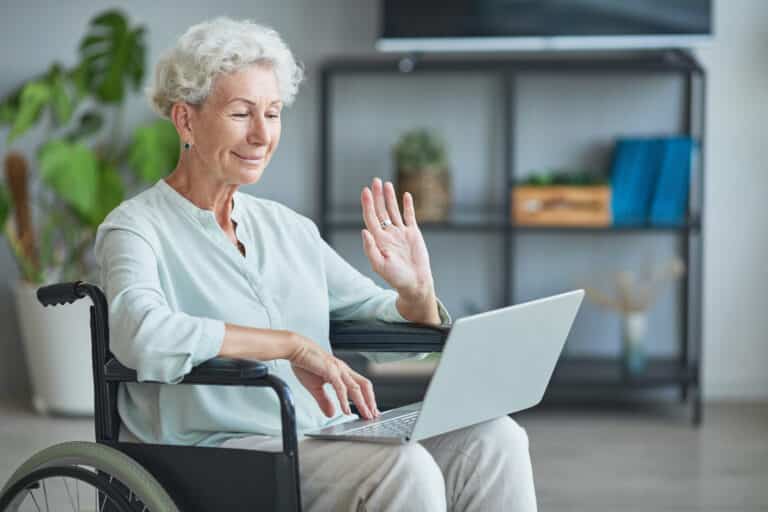 An elderly woman in a wheelchair using a laptop.