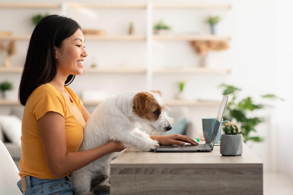A woman sitting at her desk with a dog and a laptop.