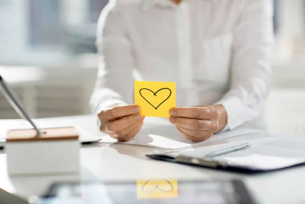 A woman holding a yellow sticky note with a heart on it.