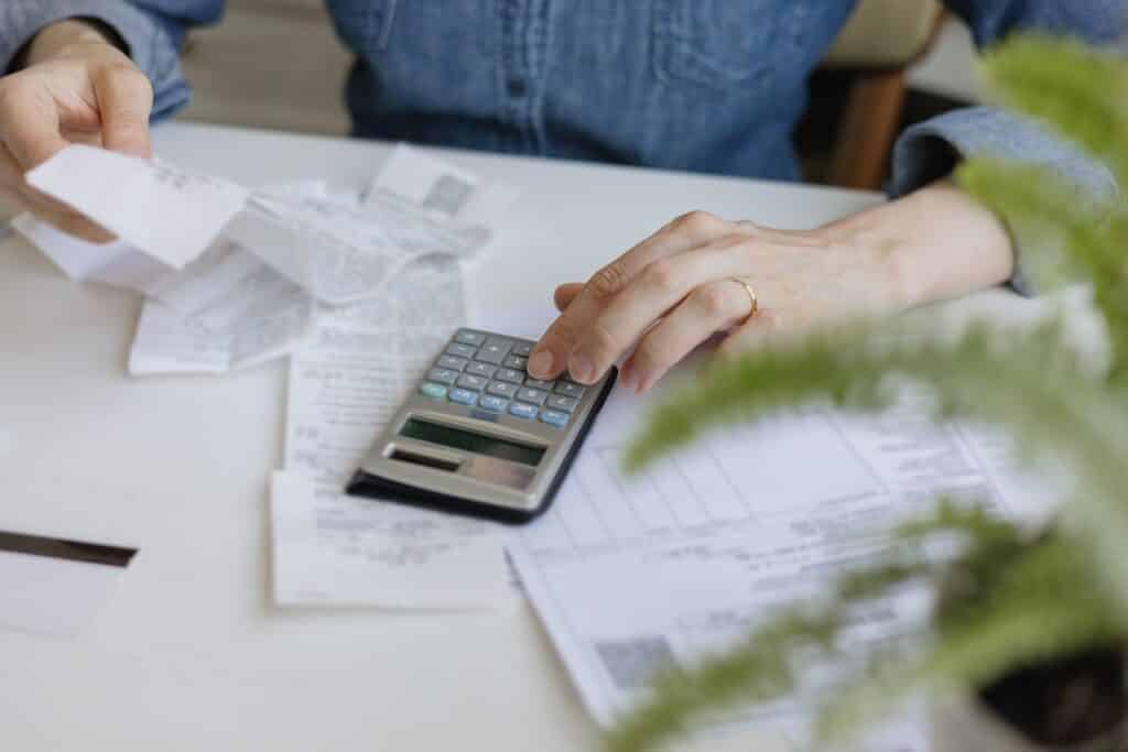 A woman is using a calculator while sitting at a table with papers.