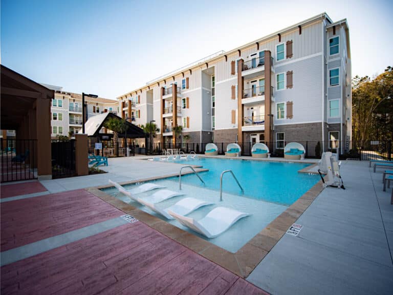 An apartment complex with a swimming pool and lounge chairs.