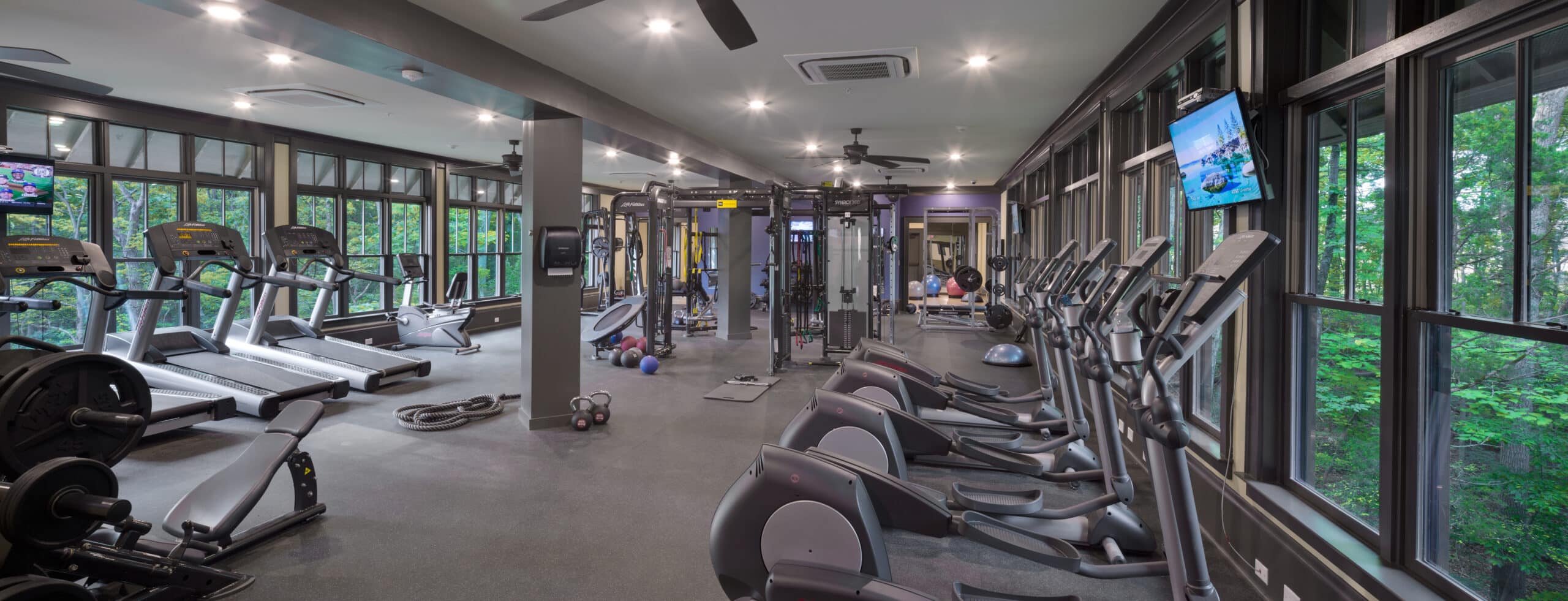 A gym with large windows and tread machines.