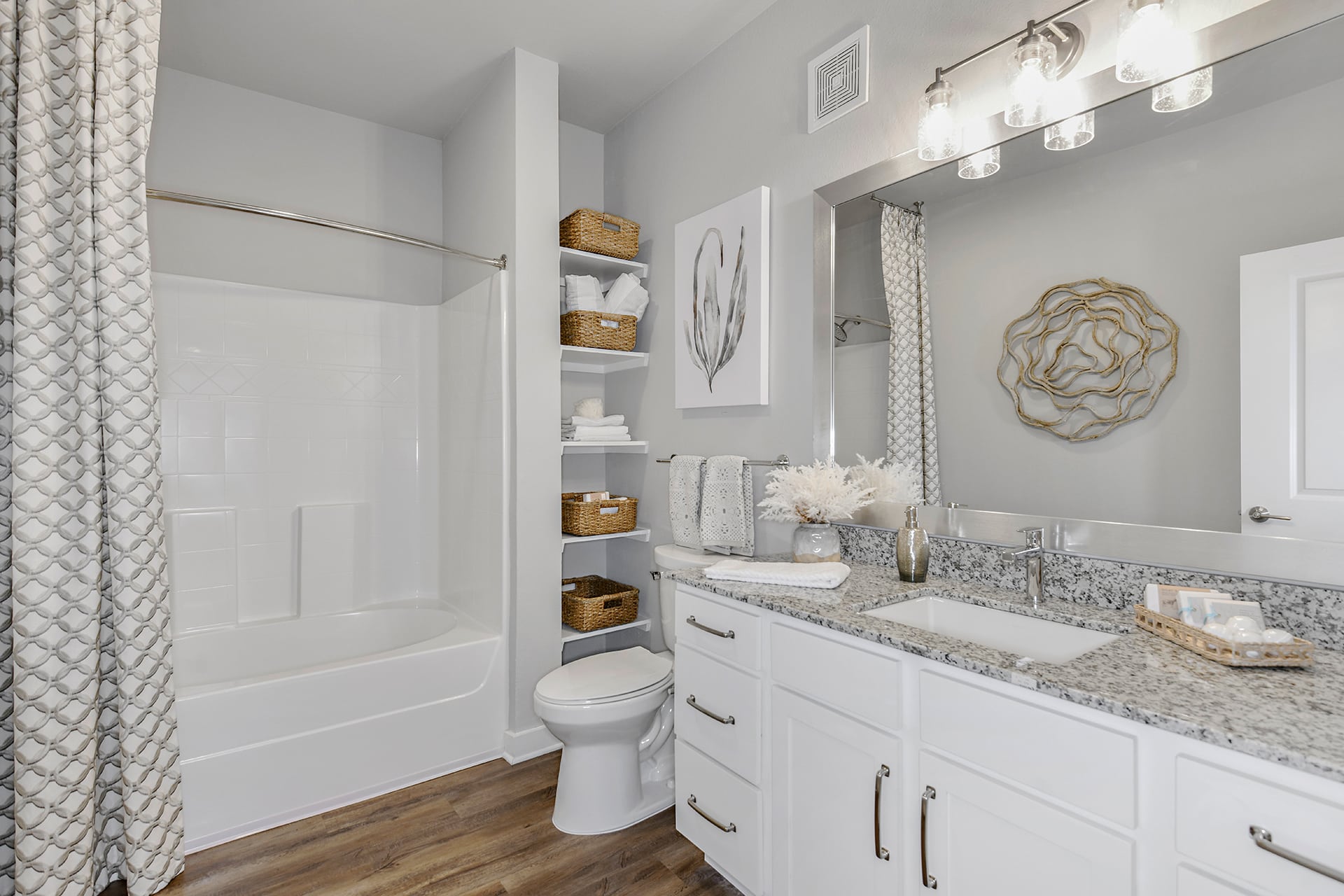 A bathroom with white cabinets and hardwood floors.