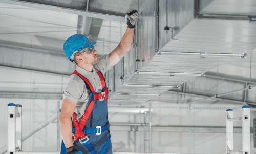 A construction worker is working on a ceiling in a warehouse.