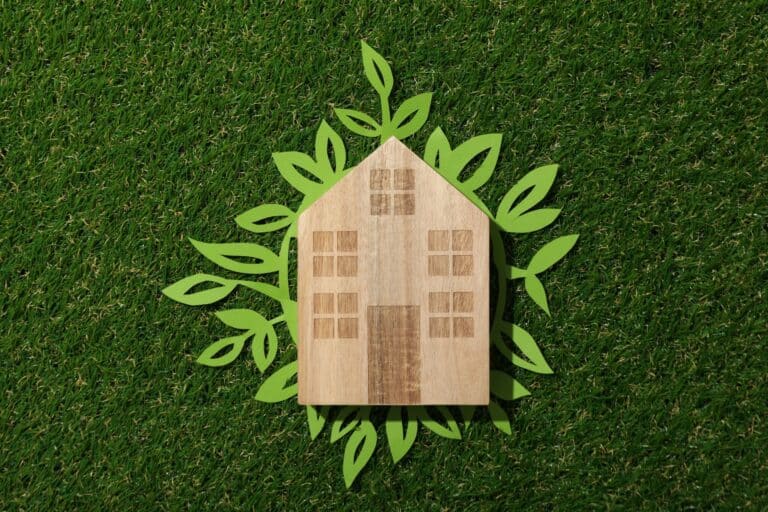 Wooden house cutout with leaf designs on a green grass background.