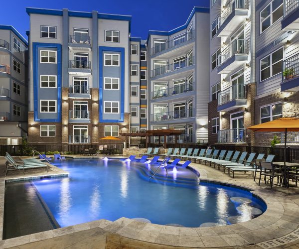 An apartment complex with a pool and lounge chairs.